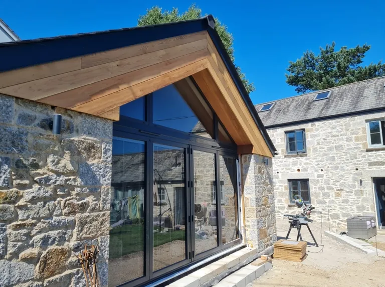 Cedar-clad gable over full-height glazing on a stone barn