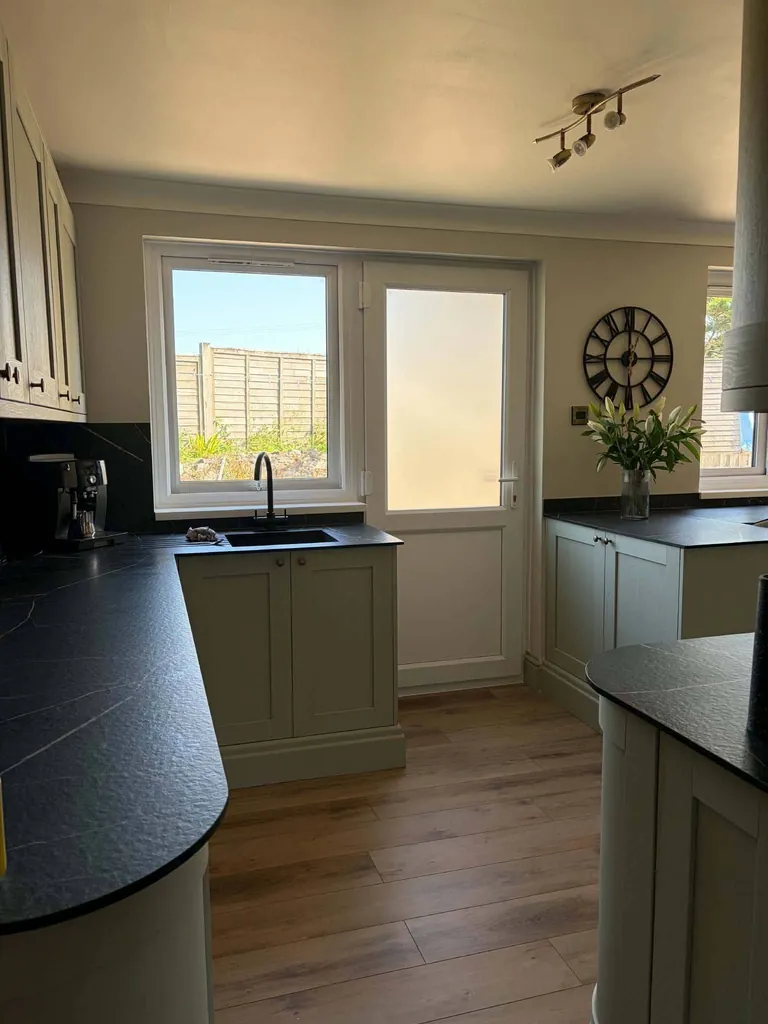 Sage shaker kitchen with curved black worktop by the back door