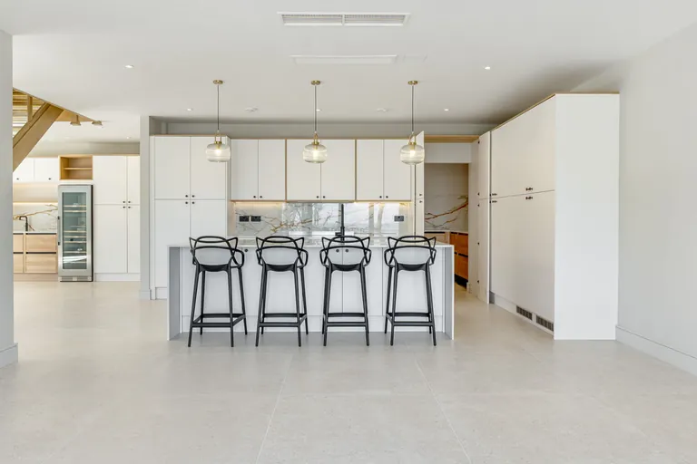 Open-plan white kitchen with island, pendant lights and tall units