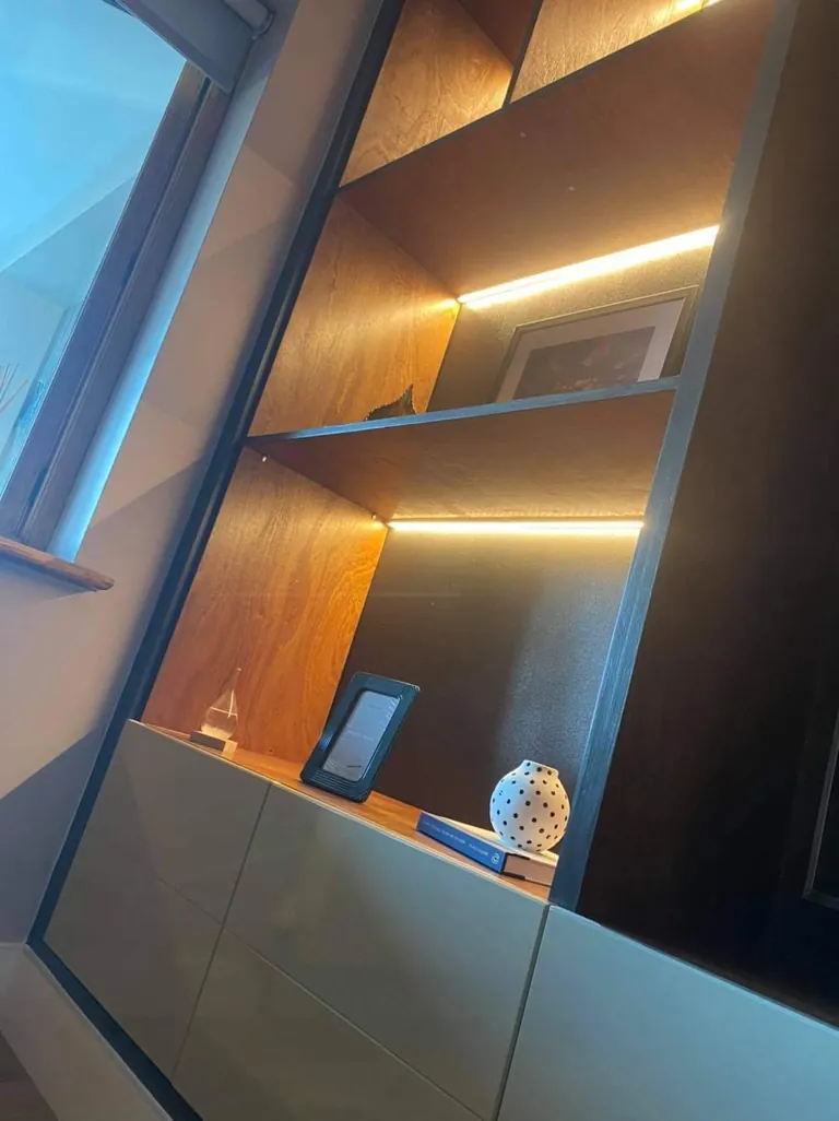 Lit oak shelving and handleless cabinets on a media wall